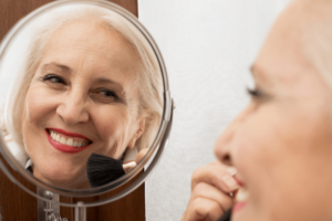 An older woman applying make up in the mirror